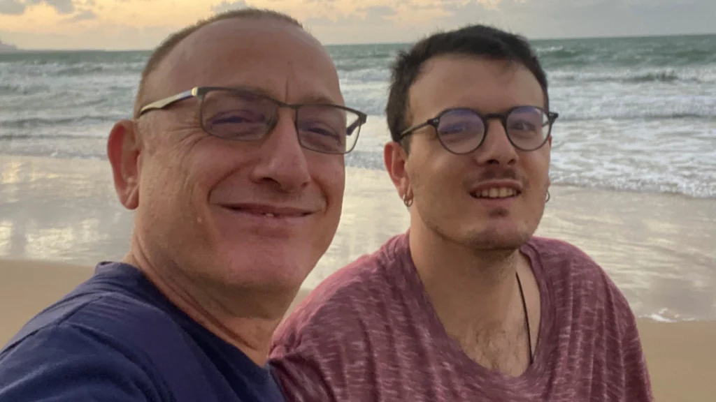 Doi bărbați zâmbitori în prim-plan, la mare